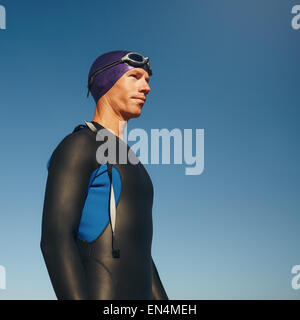 Foto von ermittelten männlichen Triathlet wegschauen gegen blauen Himmel. Junger Mann im Neoprenanzug für Triathlon wieder bereit zu tragen Stockfoto