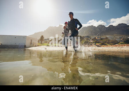 Zwei Konkurrenten im laufen ins Wasser zum Jahresbeginn einen Triathlon Neoprenanzüge. Sportler üben für das Rennen in den See. Stockfoto