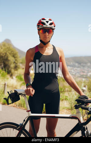 Porträt von zuversichtlich Triathletin mit ihrem Fahrrad auf der Landstraße stehen. Fitness-Frau in Sportbekleidung ansehen. Stockfoto