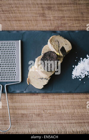 In Scheiben geschnittene Gänseleber auf eine schwarze Tafel mit schwarzem Trüffel und Meersalz Stockfoto