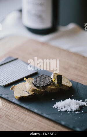 In Scheiben geschnittene Gänseleber auf eine schwarze Tafel mit schwarzem Trüffel und Meersalz Stockfoto