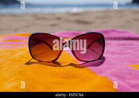 Sonnenbrille auf einer bunten Strandtuch am Sandstrand Stockfoto