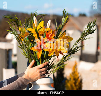 Hand legen Blumen in der Vase auf dem Friedhof. Stockfoto