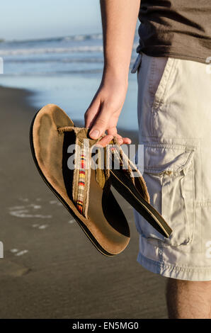 Junge Mann stand am Strand mit Pantoffeln in der hand Stockfoto