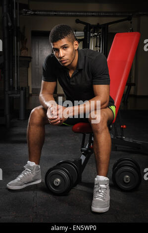 junger Mann sitzen auf Bank in Turnhalle Stockfoto