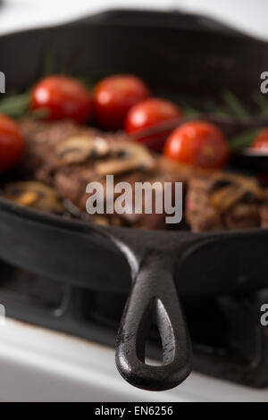 Serie: Strip Loin Steak in Gusseisen Pfanne Grillen: Steak gekocht und in Scheiben geschnitten - mit gegrillten Tomaten und Mushr Stockfoto