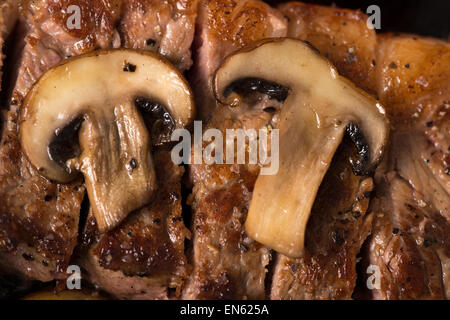 Serie: Strip Loin Steak in Gusseisen Pfanne Grillen: Steak gekocht und in Scheiben geschnitten - sautierten Pilzen in Nahaufnahme Stockfoto