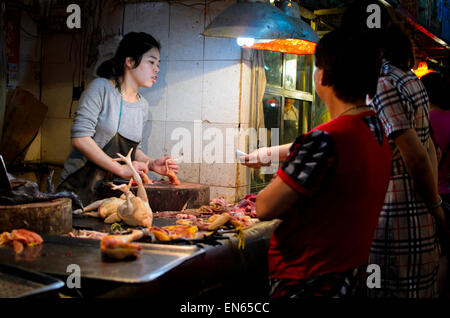 Kunde kauft frisches Geflügel aus einem jungen weiblichen Metzger in einem asiatischen Markt. Markthalle; Guangzhou, China; Frau; Frauen; Kunden Stockfoto