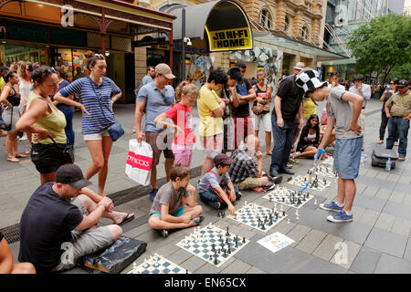 Junger Mann in einer verkehrsberuhigten Straße Simultanschach mit mehreren Personen zu spielen, während andere zusehen. Outdoor-Brettspiel; im freien; Publikum Stockfoto