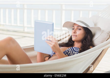 Hübsche Brünette in einer Hängematte relaxen und mit tablet-pc Stockfoto