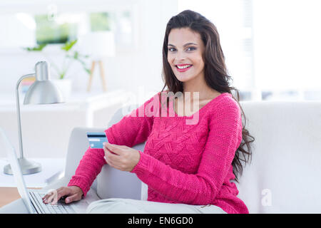 Lächelnde schöne Brünette macht Online-shopping auf der couch Stockfoto