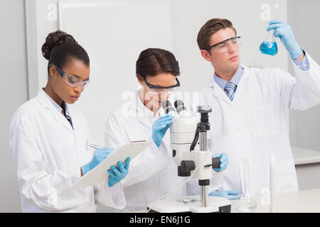 Wissenschaftler arbeiten aufmerksam mit Mikroskop und Becher Stockfoto