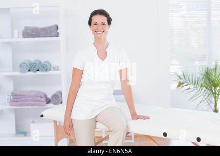 Lächelnde Arzt Blick in die Kamera sitzt auf Massagetisch Stockfoto