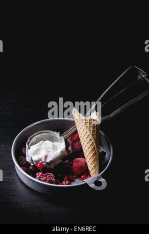 Aluminium-Platte mit Vanilleeis, Mischung aus gefrorenen Beeren und gebissen Waffer Kegel, serviert mit Metalllöffel über schwarzen Tisch Stockfoto