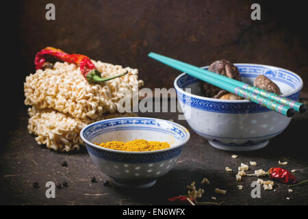 Trockene Nudeln für Ramen-Suppe mit Kurkuma Pulver und Shiitake Pilze in Porzellanschalen, serviert mit rote scharfe Chilischoten über Stockfoto
