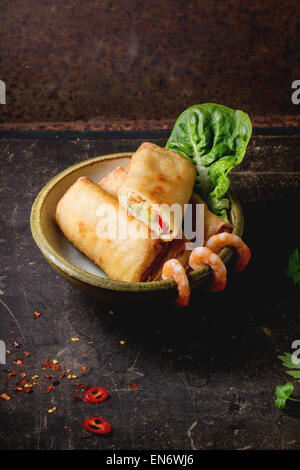 Frittierte Frühlingsrollen mit Gemüse und Garnelen, serviert in Keramikschale auf schwarzem Hintergrund. Stockfoto