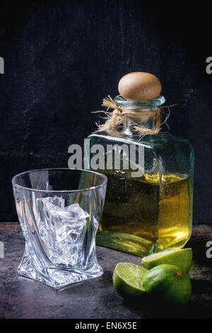 Glas mit Eiswürfeln und Flasche Tequila, serviert mit in Scheiben geschnittenen Limetten auf schwarzem Hintergrund Stockfoto