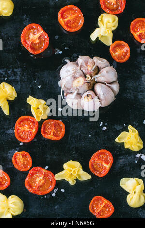 Nudeln Sacchettini und Sonne getrocknet Cherry-Tomaten mit Knoblauch und Meer Salz über schwarze Metall-Backblech. Ansicht von oben Stockfoto