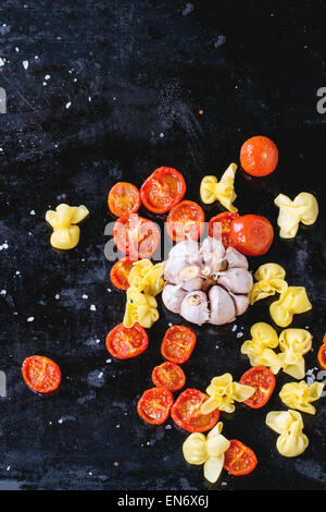 Nudeln Sacchettini und Sonne getrocknet Cherry-Tomaten mit Knoblauch und Meer Salz über schwarze Metall-Backblech. Ansicht von oben Stockfoto