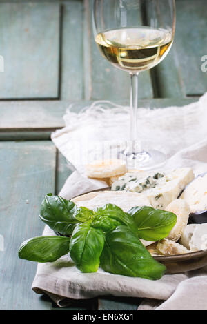 Variation von Käse, serviert mit frischem Basilikum, Brot und Glas Weißwein über Türkis Holztisch. Serien ansehen Stockfoto