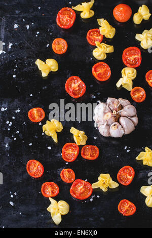 Nudeln Sacchettini und Sonne getrocknet Cherry-Tomaten mit Knoblauch und Meer Salz über schwarze Metall-Backblech. Ansicht von oben Stockfoto