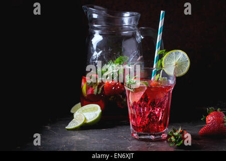 Glas mit Retro-Coctail Röhren und Glaskanne Erdbeer Limonade, serviert mit frischen Erdbeeren, Minze und Limette über dunkle ba Stockfoto