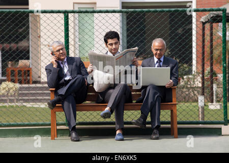 Junge männliche Führungskraft Zeitunglesen beim sitzen unter den Führungskräften auf Bank, DELHI, Indien Stockfoto