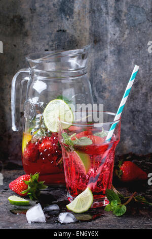 Glas mit Retro-Coctail Röhren und Glaskanne Erdbeer Limonade, serviert mit frischen Erdbeeren, Minze und Limette über dunkle ba Stockfoto