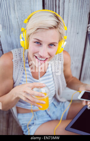 Hübsche blonde Frau mit ihrem Handy Musik hören und trinken Orangensaft Stockfoto