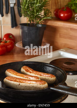 Drei Würste gebraten in Gusseisen Pfanne, Tomaten und Küche Tabelle auf Hintergrund Stockfoto