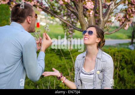 Großer Kerl und Brünette Mädchen bläst Löwenzahn im park Stockfoto