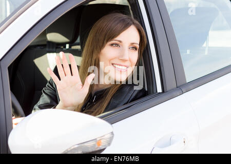 Junge lächelnde Frau Gruß mit der Hand aus dem Auto. Fröhliches kaukasisches Mädchen begrüßen jemanden im Auto sitzen Stockfoto