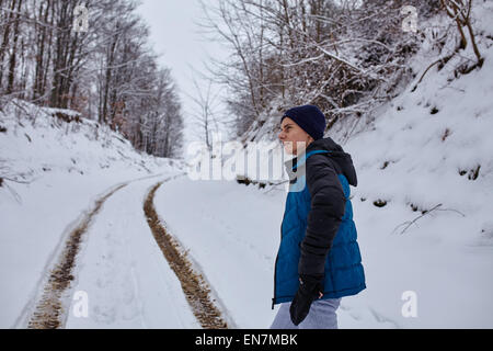 Teenager auf einer verschneiten Landstraße durch den Wald wandern Stockfoto