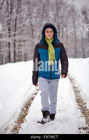 In voller Länge Portrait von Teenager zu Fuß auf eine verschneite Land Straße durch den Wald Stockfoto