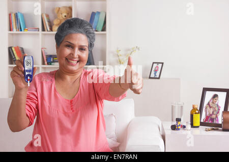 Alte Frau mit Blutzuckermessgerät Daumen aufgeben Stockfoto