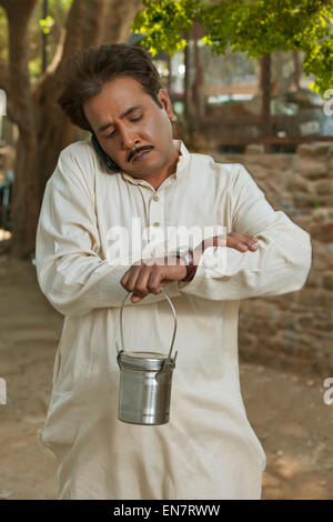 Mann am Handy sprechen und halten Milch Kanister Blick auf Uhr Stockfoto