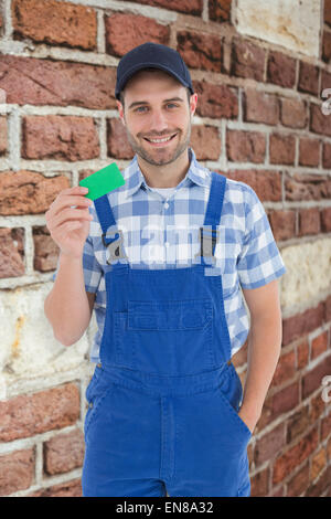 Zusammengesetztes Bild des lächelnden jungen Mechaniker mit Green card Stockfoto