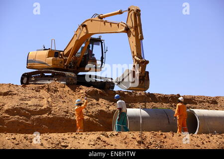 Bagger, die Unterstützung der Arbeiter verlegen Rohre aus Beton auf der Baustelle Stockfoto
