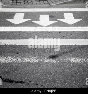 Weiße Pfeile und Linien auf dunklem Grau Asphaltstraße, Fußgängerüberweg Kennzeichnung Stockfoto