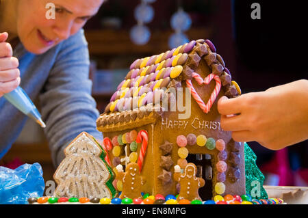 Horizontale Ansicht ein Lebkuchenhaus wird durch eine Mutter und Tochter zu Weihnachten dekoriert. Stockfoto