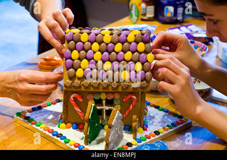 Horizontale Ansicht ein Lebkuchenhaus wird durch eine Mutter und Tochter zu Weihnachten dekoriert. Stockfoto