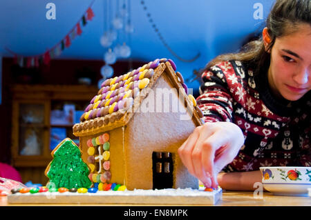 Horizontale Ansicht ein Lebkuchenhaus wird von einem jungen Mädchen zu Weihnachten dekoriert. Stockfoto
