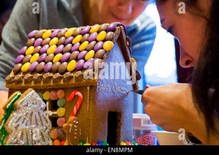 Horizontale Ansicht ein Lebkuchenhaus wird durch eine Mutter und Tochter zu Weihnachten dekoriert. Stockfoto