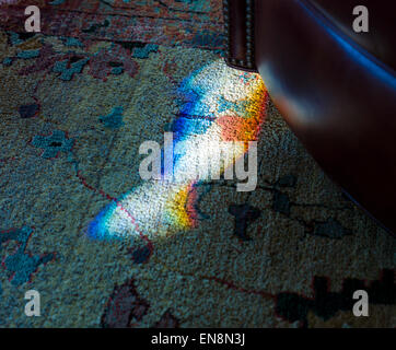Ende Tag Sonnenlicht gebrochen durch einen gefärbten, verbleiten Fenster schafft eine Prisma von Farbe auf dem Teppich Stockfoto