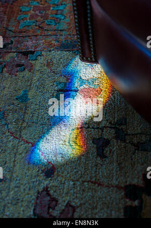 Ende Tag Sonnenlicht gebrochen durch einen gefärbten, verbleiten Fenster schafft eine Prisma von Farbe auf dem Teppich Stockfoto