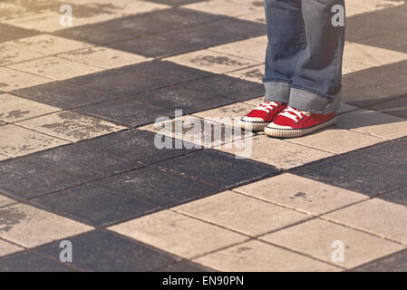 Beine des jungen Teenager weiblich in Red Sneakers stehen auf der Straße im Schach wie karierte Pflaster, getönten Bild mit Selective Stockfoto