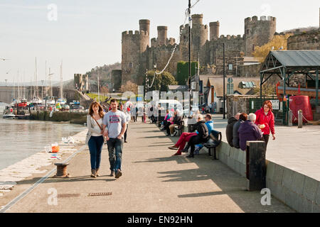 Besucher genießen die Frühlingssonne auf Conwy Quay, mit Conwy Castle im Hintergrund Stockfoto