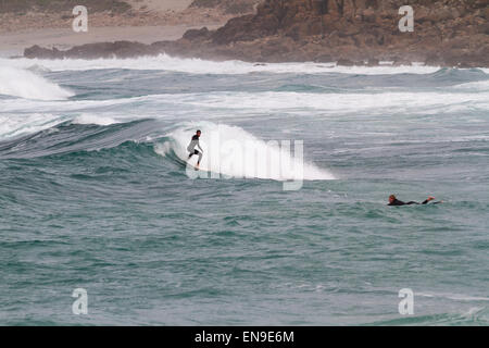 SENNEN COVE, CORNWALL, ENGLAND - 22. Oktober 2014: Surfer fangen eine Welle an einem kalten Herbsttag am 22. Oktober 2014 in Sennen Co Stockfoto