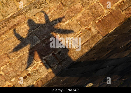 Gemauerte Wand Sonne Licht werfen Schatten über es, drei Personen standen Schlange, um den gleichen Schatten Armen gestemmt gegossen ausgestreckt. Stockfoto