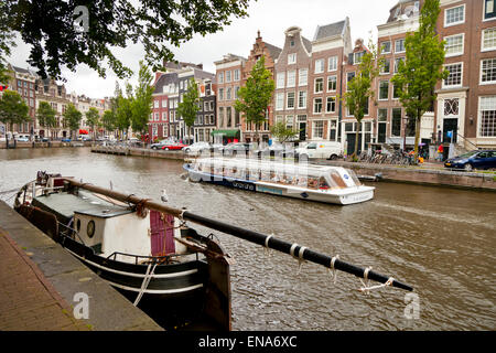 Ein Ausflugsschiff geht durch ein Schiff vor Anker an einer Gracht in Amsterdam Stockfoto